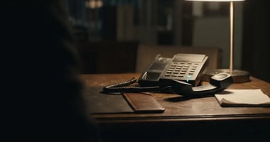 A desk phone with its handset lifted off the cradle on a wooden desk at night